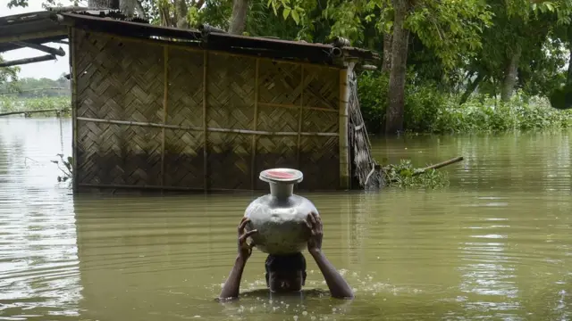 A man walks through deep water carrying a vase on his head