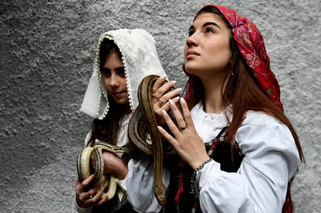 Faithfuls in traditional clothing hold snakes to place them on the statue of Saint Domenico during an annual procession in the streets of Cocullo