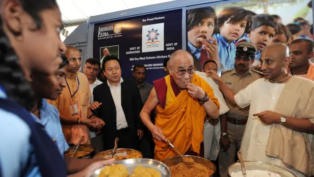 Духовный лидер буддистов Далай-лама XIV пробует еду для школьников в Бангалоре, Индия, июль 2013 года.