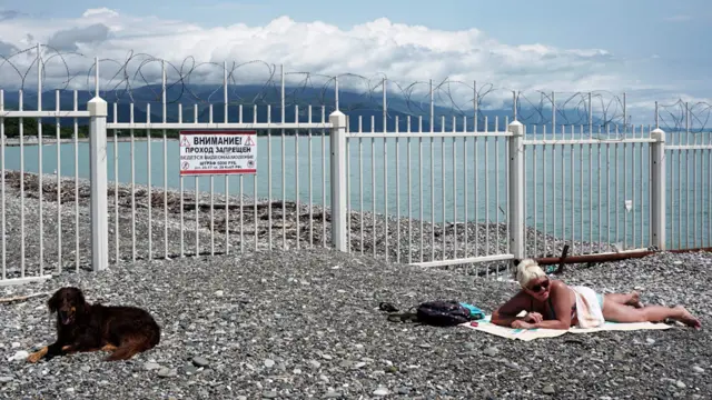 Žena i njen pas se sunčaju kraj granice Crnog mora između Rusije i Abhazije