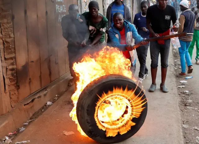 A man hits a flaming tyre with a stick