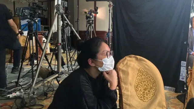 Moon Tsui watching a film shoot with cameras and lights in the background