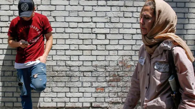 A man uses his mobile phone as a woman walks by in Tehran, Iran (8 July 2019)