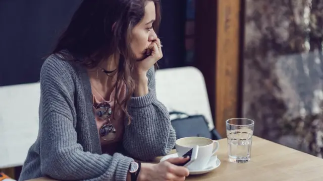 Una mujer depresiva y pensativa con un teléfono en la mano.
