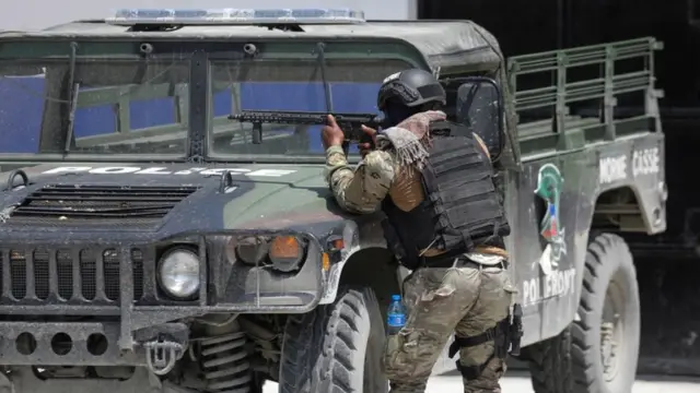 Un miembro de la Policía Nacional de Haití se protege detrás de un vehículo policial mientras patrulla, foto tomada el 28 de abril de 2022.