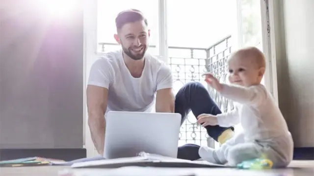 Father working on laptop and watching baby