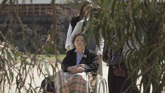 Teruko en silla de ruedas empujada por Tomoko en el jardín de Shukkeien