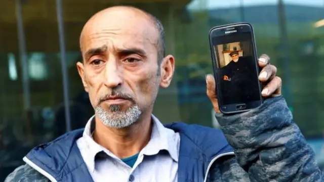 Omar Nabi na telefone igaragaza ifoto ya se Daoud, imbere y'icyumba cy'urukiko kuri uyu wa gatandatu