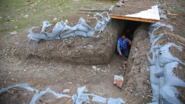 Two people crouch in a trench covered by wood and earth