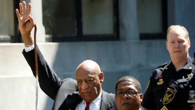 Bill Cosby levantando la mano a la salida del juzgado luego de haber sido declarado culpable.