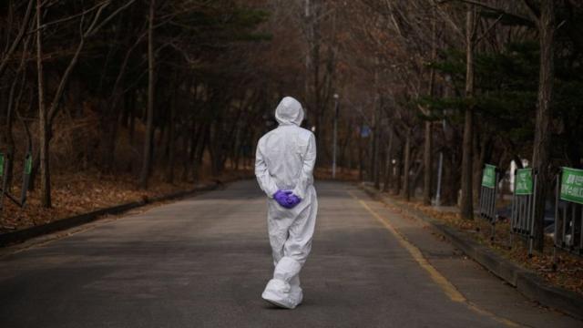 Um profissional de saúde vestindo um traje de proteção caminha sozinho em uma estrada vazia