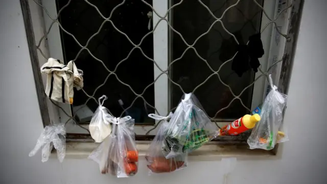 Zanahoria, queso y algunas legumbres cuelgan en bolsas plásticas de una ventana enrejada.