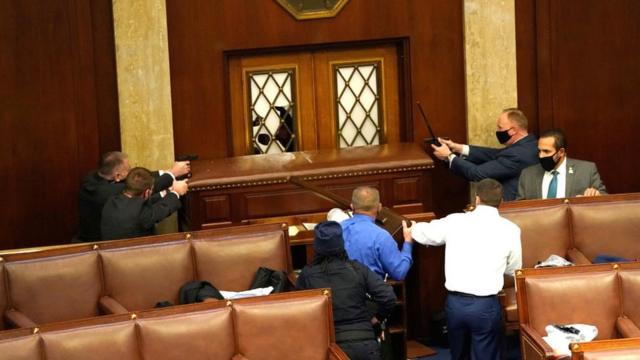 Law enforcement officers point their guns at a door that was vandalised in the House Chamber during a joint session of Congress in Washington DC, 6 January 2021