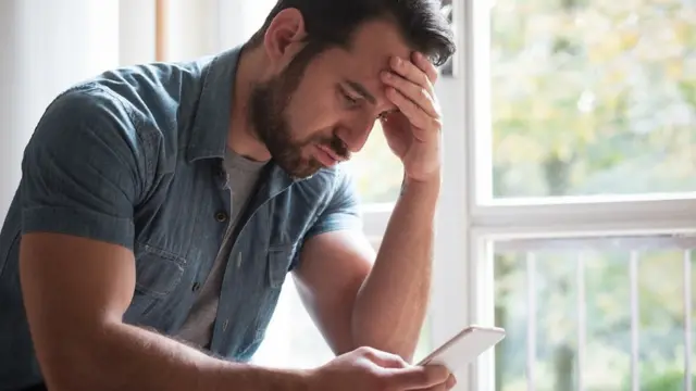 বিষন্ন এক ব্যক্তি বাড়িতে একা একটি ফোন হাতে বসে আছেন