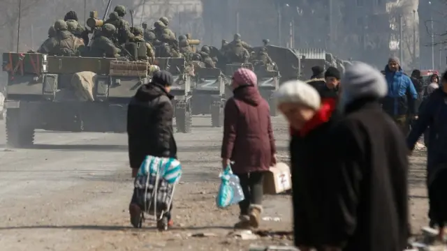 Service members of pro-Russian troops drive armoured vehicles past local residents in the besieged southern port city of Mariupol