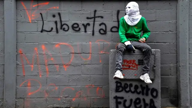 Protestante enmascarado delante de un grafiti que dice: "Libertad".