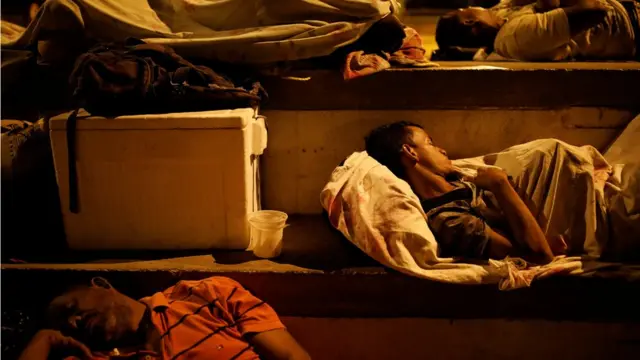 Hombres duermen encima de sábanas en el piso de un centro deportivo.