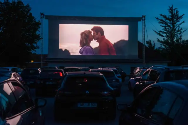 Olivia Newton-John y John Travolta como Sandy Olsson y Danny Zucko en una escena de "Grease", película de 1978, proyectada en un autocine en 2020.