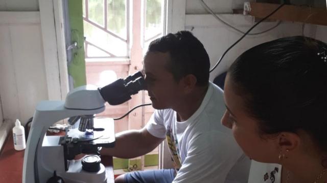 Homem observa lâmina de exame de malária no microscópio, em um barco equipado para fazer atendimento de saúde em Bagre (PA)