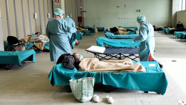 Medical personnel wearing protective face masks help patients inside the Spedali Civili hospital in Brescia, Italy, 13 March 2020