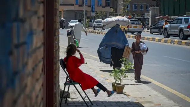 امرأة ترتدي البرقع وتحمل كيسًا على رأسها تمشي على طول طريق في كابول في 7 أغسطس 2021