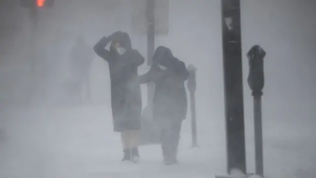 pessoas tentam se proteger da neve e do vento