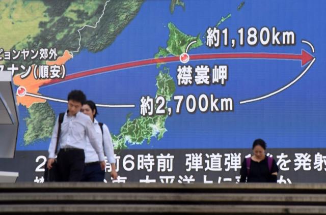 在东京街头，行人走过展示有日本和朝鲜半岛地图的巨大屏幕。