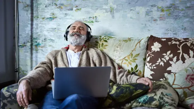 Homem sentado no sofá com laptop no colo ouvindo música