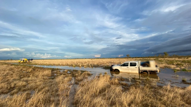 The rescue helicopter a short distance away from the ute bogged in floodwaters