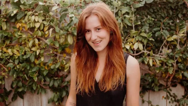 Kate Hall debout contre un mur de feuillage