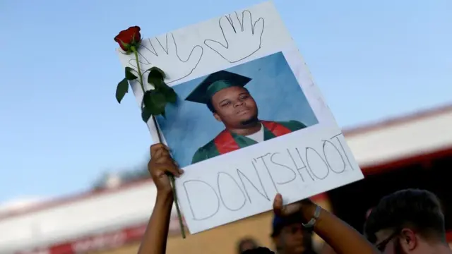 أحد المتظاهرين يرفع صورة مايكل براون الذي قُتل عن عمر يناهز 18 عاما برصاص ضابط شرطة في مدينة فيرغسون بولاية ميزوري في عام 2014