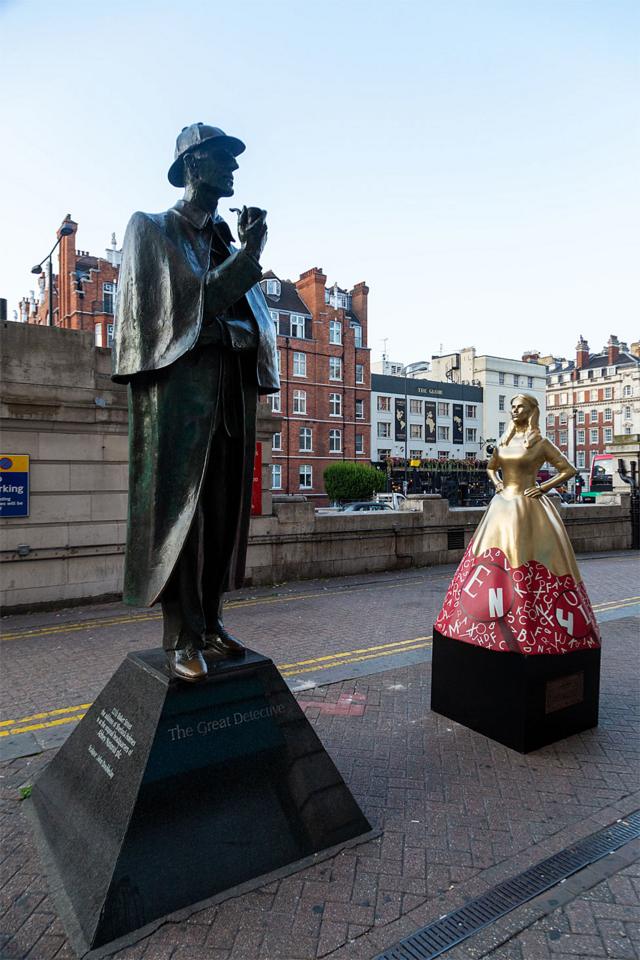 Enola em frente à estátua de seu irmão Sherlock Holmes