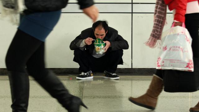 Homem come macarrão instantâneo sentado no chão
