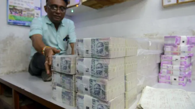 दो हज़ार और एक सौ रुपए के नए नोट के साथ एक व्यक्ति.