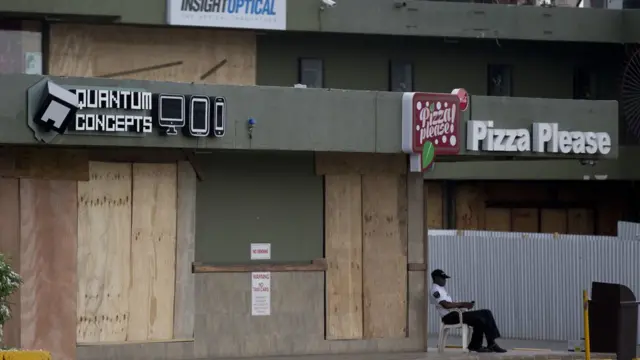 Afisa mlinzi asimama karibu na maduka yaliyofunikwa kwa kutumia mbao, kabla ya kuwasili kwa kimbunga Mathew mjini Kingston, Jamaica, Jumatatu Okt. 3, 2016