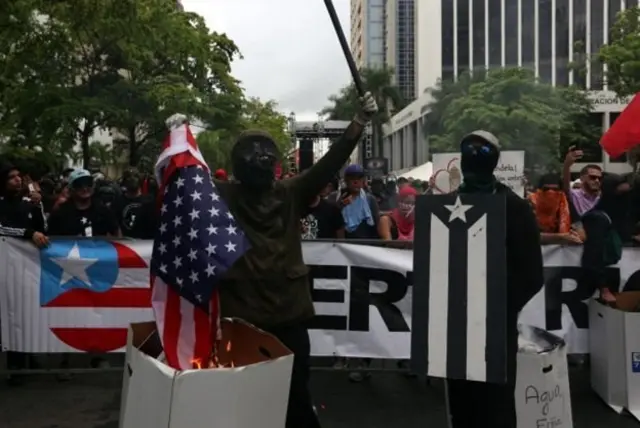Hombres enmascarados prenden fuego la bandera de Estados Unidos.