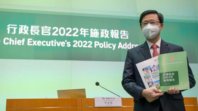 李家超在香港特区政府总部记者会上举起施政报告文本予媒体记者拍照（中新社图片19/10/2022）