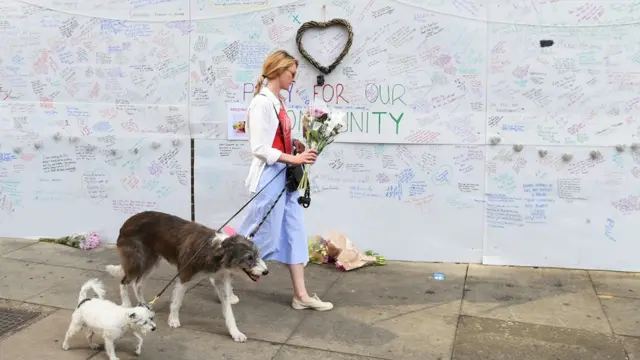 A woman carrying flowers past a wall of messages