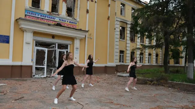 Four female students dancing in front of their school ruins