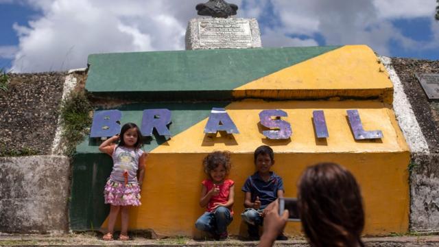 Crianças venezuelanas posam para uma foto em frente a um monumento em Pacaraima que diz "Brasil", com as cores do país