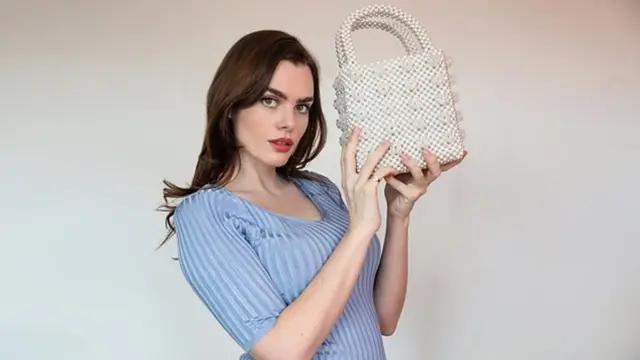 Charli holding a white beaded handbag - light grey background
