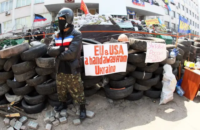 Fotografia mostra homem com capuz cobrindo o rostogratis betsfrente a uma barricada feita com pneus