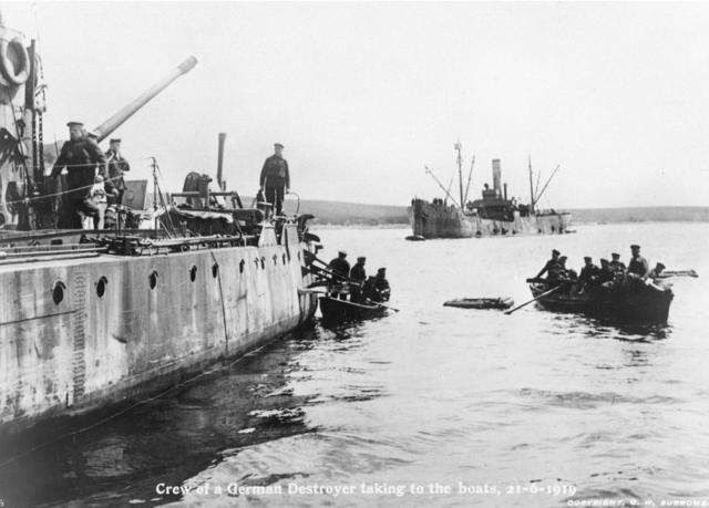 德国一艘驱逐舰上的官兵在凿船自沉后乘搭小木船弃船离开。