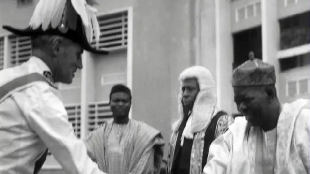 Ọba Adesoji Tadenikawo Aderemi n bọ oyinbo kan lọwọ