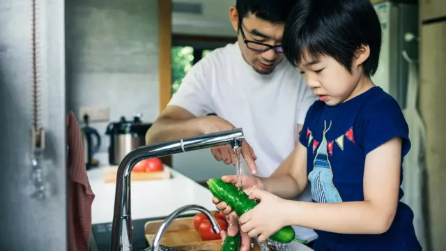 Père et fils lavant des fruits frais dans l'évier de la cuisine.