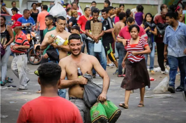 एक सुपरमार्केट से लूटपाट के बाद सामान ले जाते लोग.
