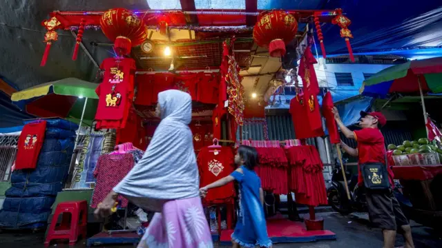 People walk past a kiosk selling Chinese-style decorations and T-shirts for the Lunar New Year in Jakarta on February 16, 2018