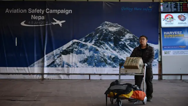 কাঠমান্ডুর ত্রিভুবন বিমানবন্দর নিরাপত্তা সপ্তাহ পোস্টারের সামনে একজন অপেক্ষমাণ যাত্রী।