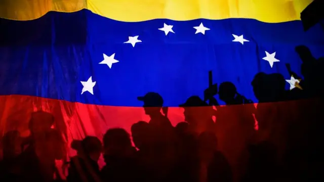 Bandera de Venezuela con personas protestando a contraluz.