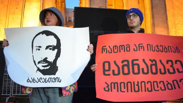 Плакаты в руках участников акции. На одном - изображение актера Гиорганашвили, на втором - надпись: "Почему не наказывают виновных полицейских?"